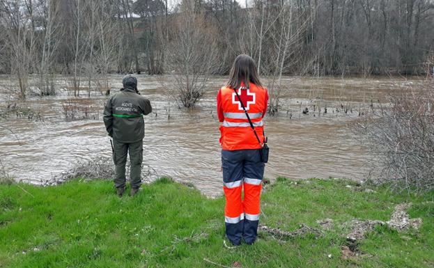 Un agente medioambiental y una voluntaria de Crus Roja observan resignados el desbordado caudal del Arlanza