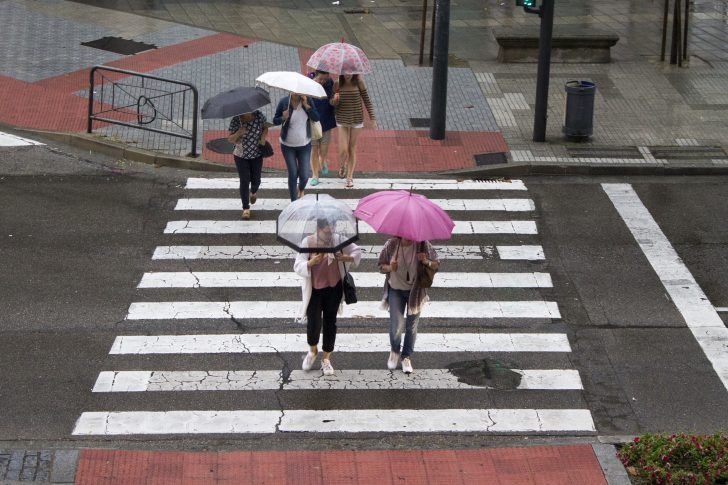 Varias mujeres cruzan un paso de peatones protegidas por paraguas.