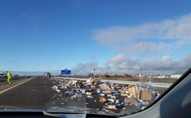 Imagen de las cajas con el pan de molde esparcidas por la carretera y el camión al fondo. 