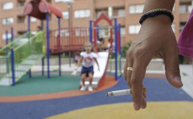 Un fumador sostiene un cigarrillo en un parque infantil, algo que está prohibido en España por ley.