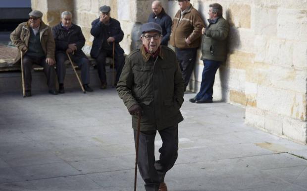 Un señor pasea por una plaza ante un grupo de mayores reunidos en la misma zona