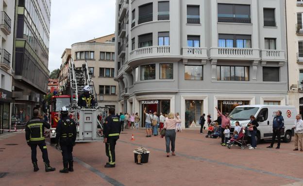 Imagen principal - Viandantes observando la medianera (centro), los bomberos bajan un cubo con cascotes (izquierda) y aspecto de la pared (derecha).