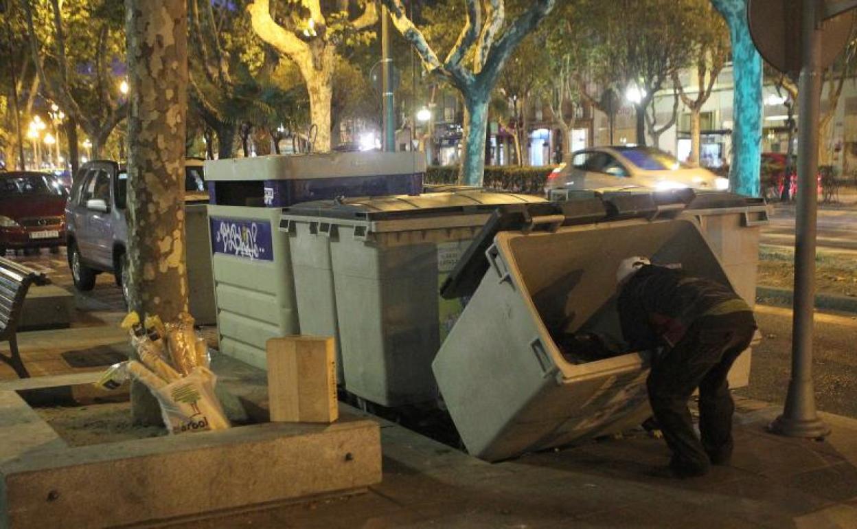 Una persona busca comida en un contenedores de basura.