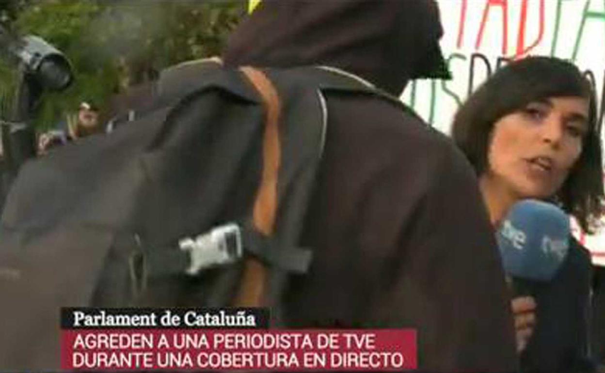 La periodista trata de seguir informando a pesar de que un encapuchado quiere impedírselo.