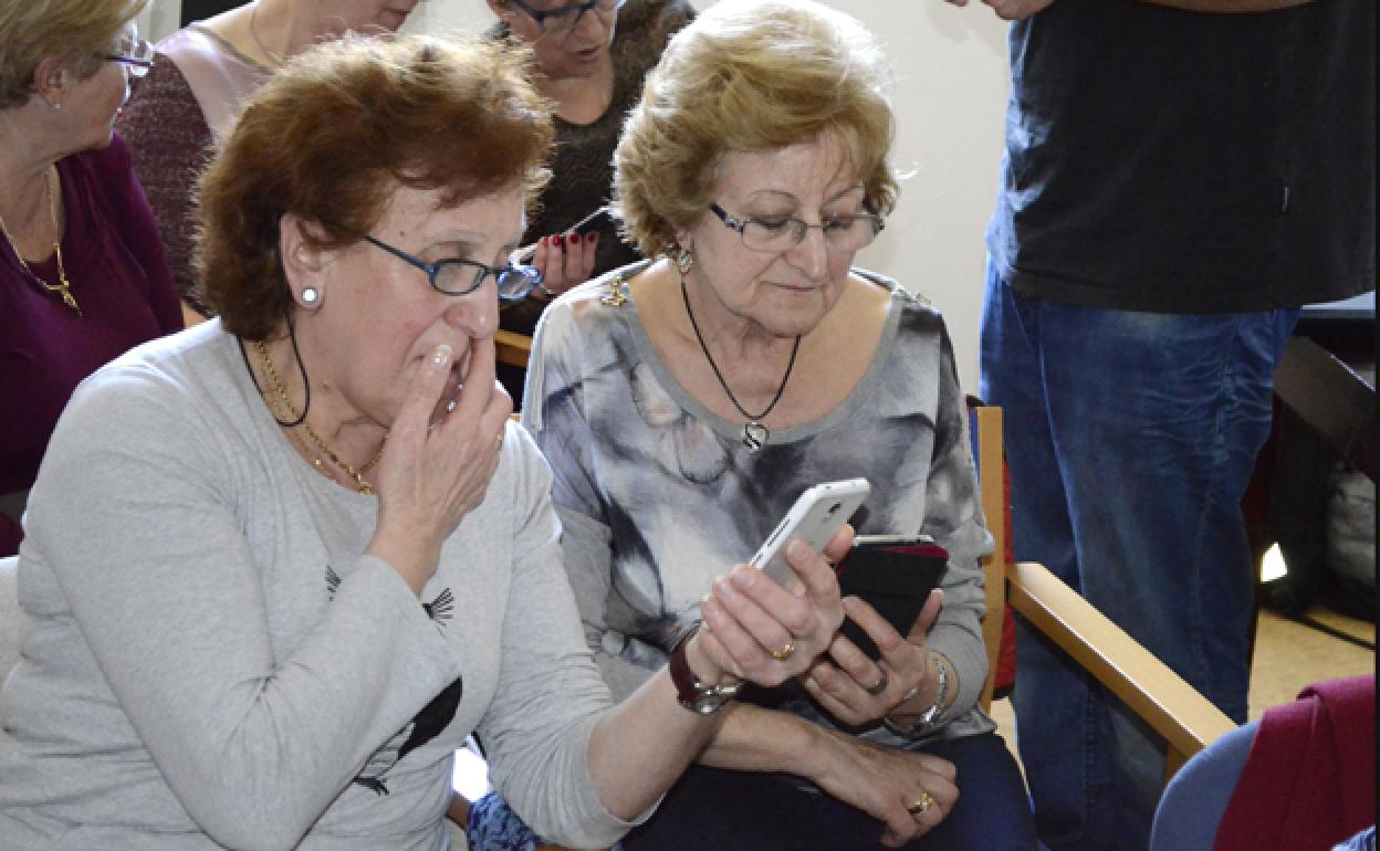 Dos personas mayores observan sus respectivos móviles. 