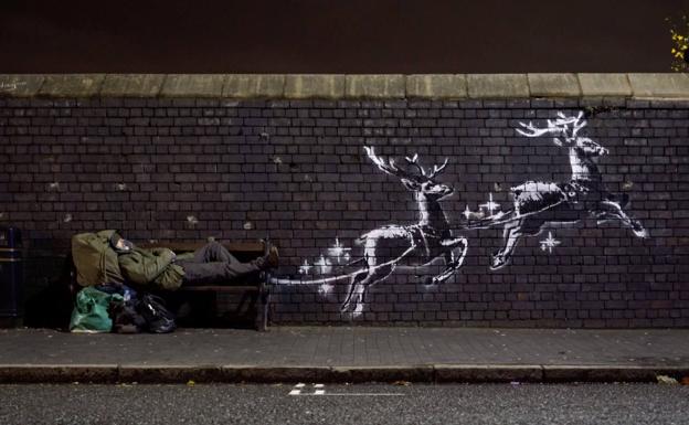Un hombre sin hogar yace en un banco junto a un nuevo mural de Banksy en Birmingham, Gran Bretaña.
