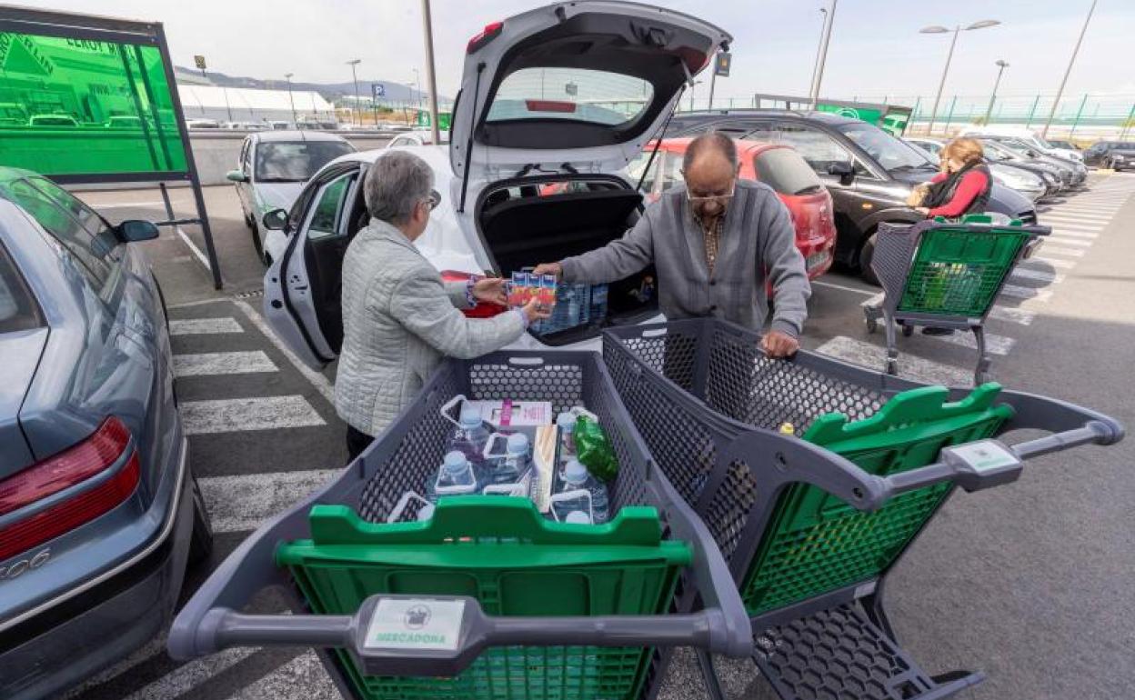 Dos personas cargan su coche con todos los productos que han comprado en un hipermercado.