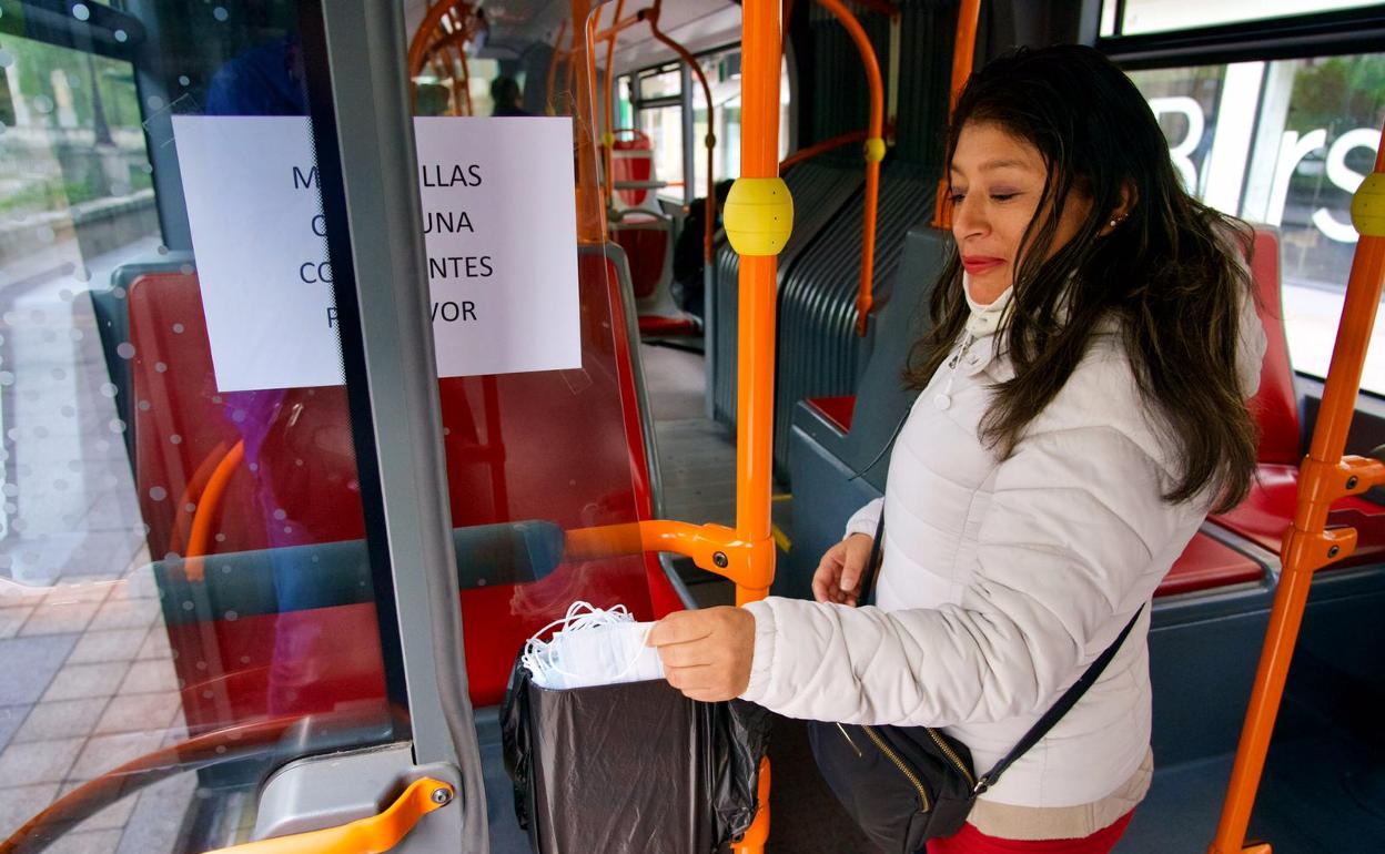 Una usuaria del transporte urbano recoge una mascarilla en el autobús. 