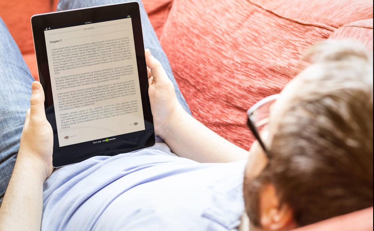 Un hombre leyendo un libro en un dispositivo electrónico.