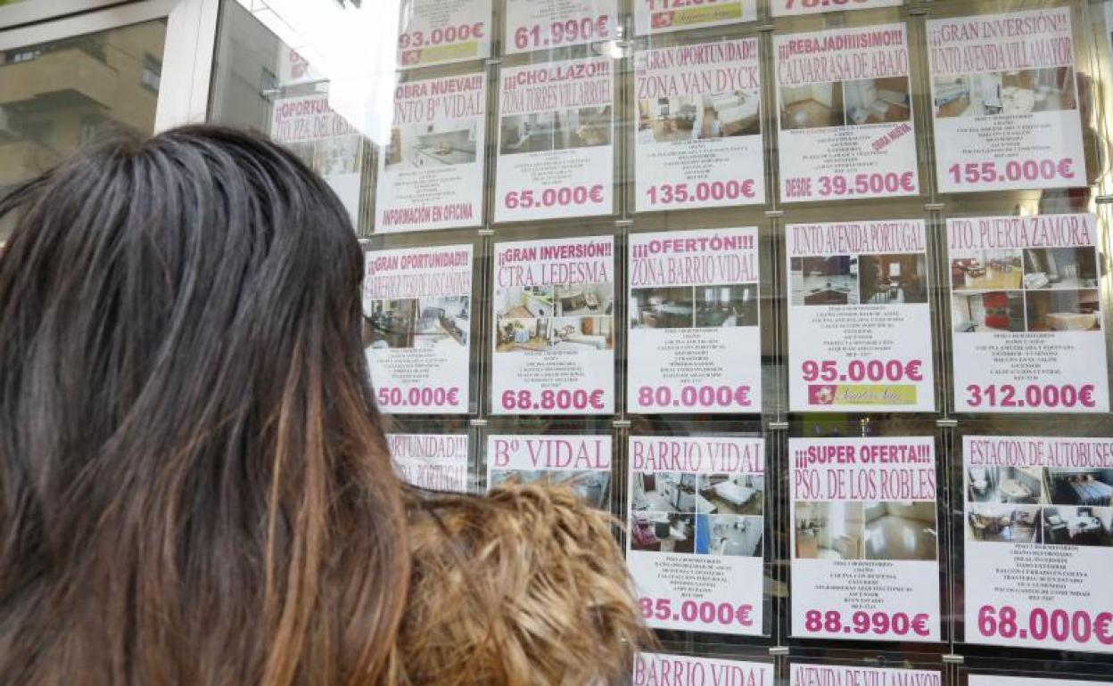 Una joven observa los anuncios de viviendas en venta en el escaparate de una inmobiliaria.