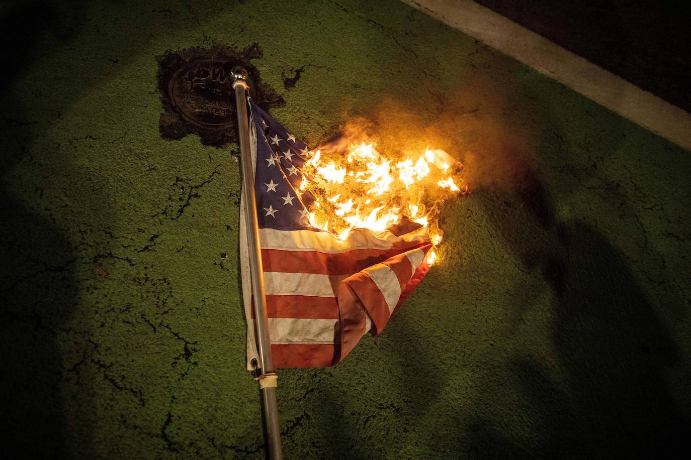 Una bandera de EE. UU. Yace en el suelo ardiendo durante una protesta después de las elecciones presidenciales de EE. UU.