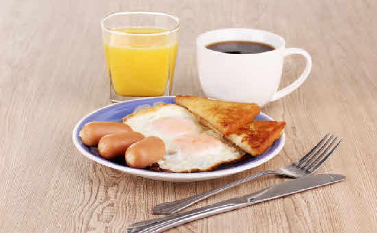 Desayuno a base de huevos fritos con salchichas, tostadas, zumo y café 