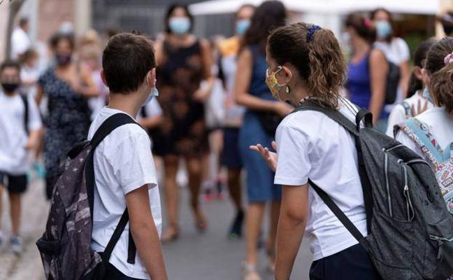 Dos niños con mascarilla esperan en la salida del colegio.