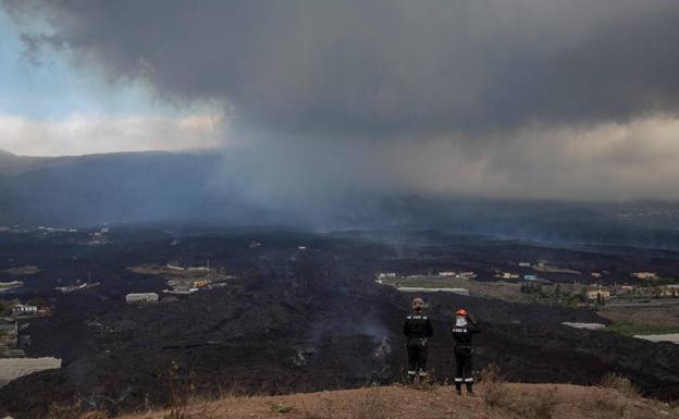 Dos operarios frente al volcán de Cumbre Vieja, en La Palma.