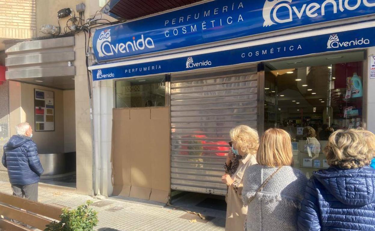 Los vecinos se arremolinan en la puerta del establecimiento, que permanece cerrado al público y con el agujero del escaparate tapado con un cartón.