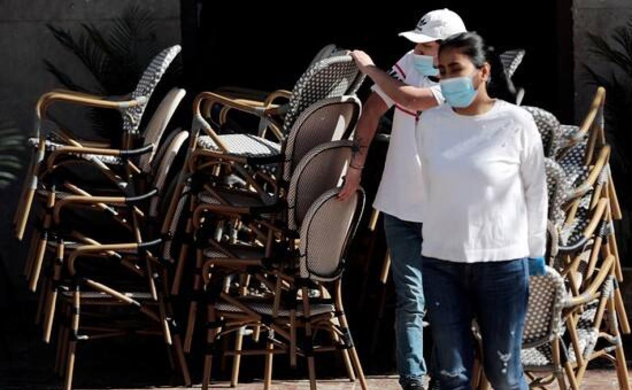 Un camarero y una camarera trabajan montando la terraza de un local. 