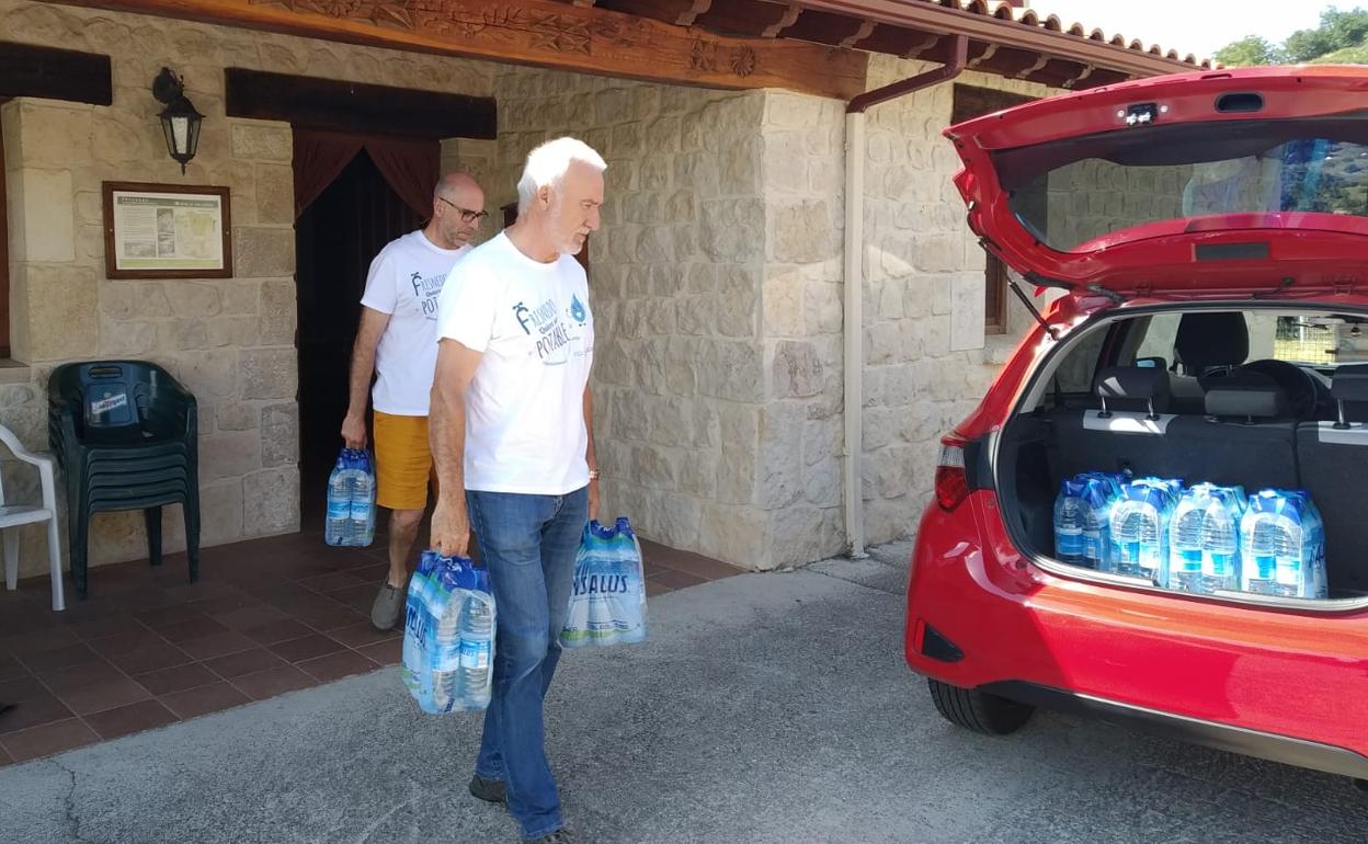 Dos vecinos de Fresnedo acuden a la Casa del Concejo a recoger el agua embotellada que les suministran al no poder consumir agua del grifo. 