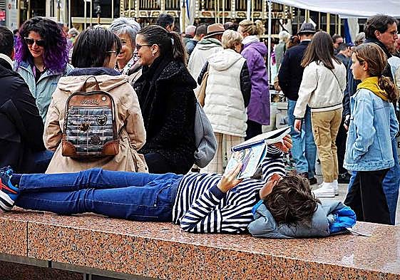 Un niño lee un libro en la plaza Mayor de Burgos donde se encontraba la feria por el Día del Libro.