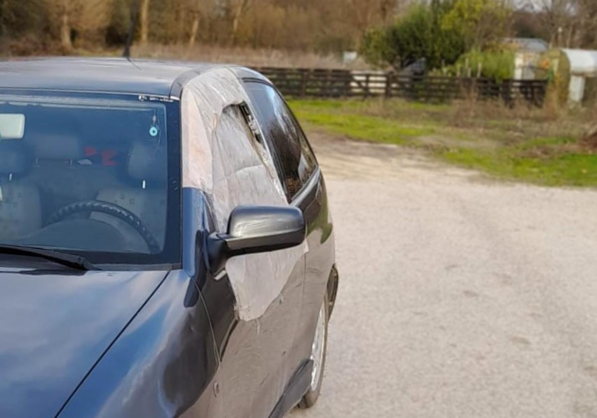 Uno de los coches que ha sufrido daños con la ventanilla rota y protegida por plásticos.