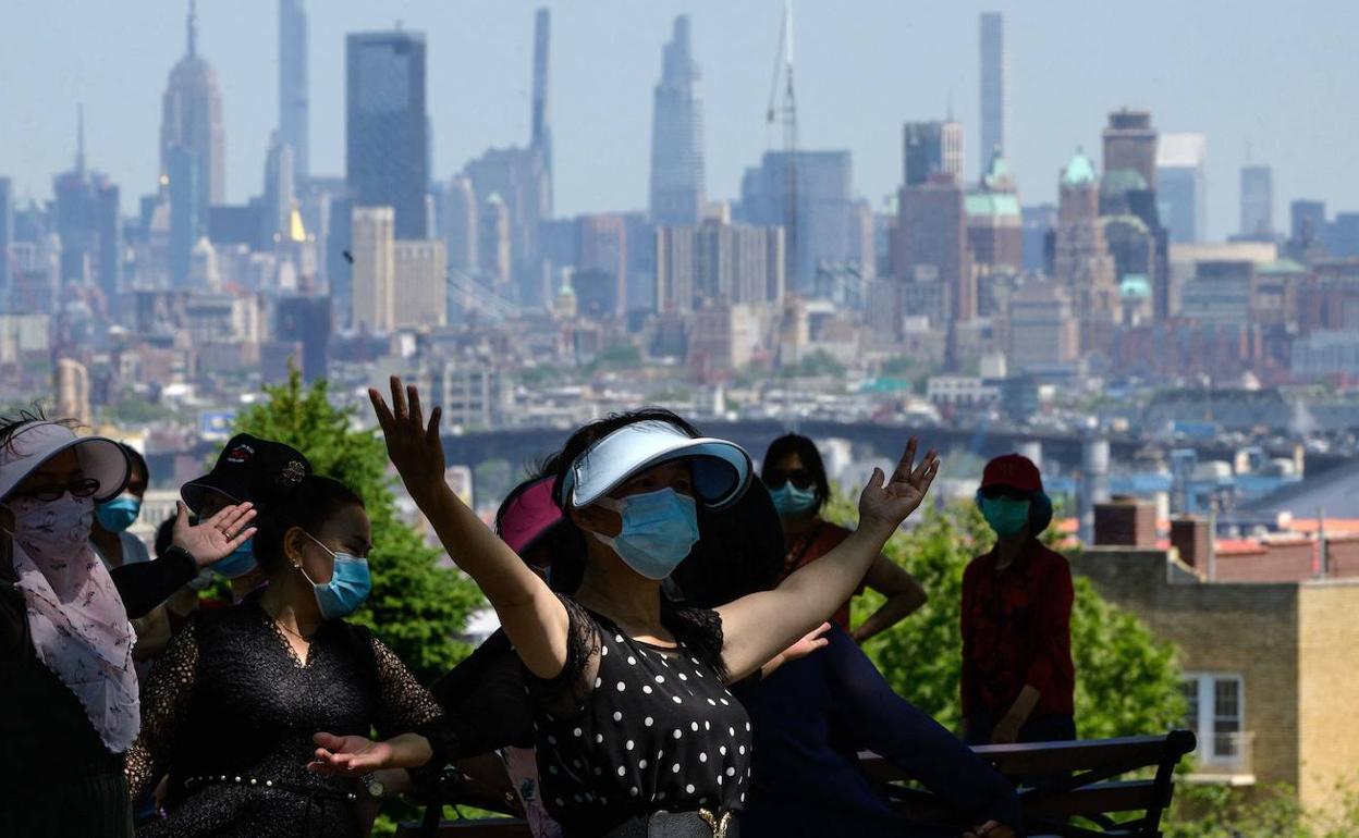 Turistas con mascarillas por la covid-19 en un parque de Nueva York con Manhattan al fondo.