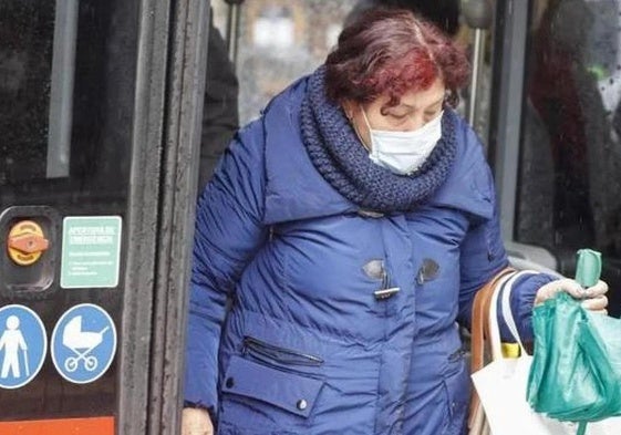 Una mujer baja del bus urbano con mascarilla.