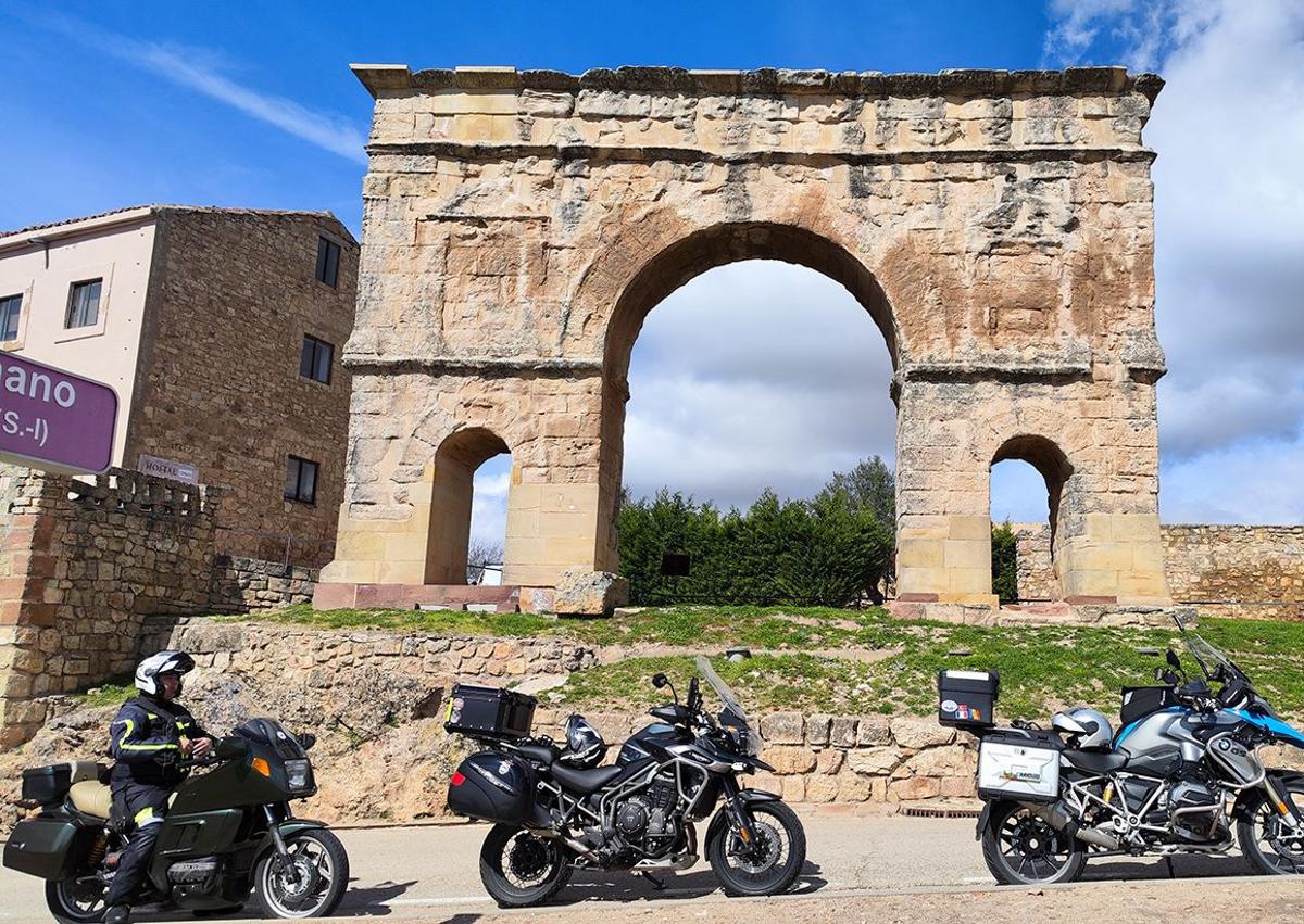 Imagen secundaria 1 - Arriba, motoristas junto a la Estatua del Cid en Mecerreyes; abajo, a la izquierda, en el Arco romano de Medinaceli y a su lado en la plaza Mayor de Sigüenza, Guadalajara.