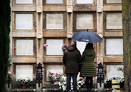 Dos personas frente a los nichos con flores en el cementerio de Burgos.