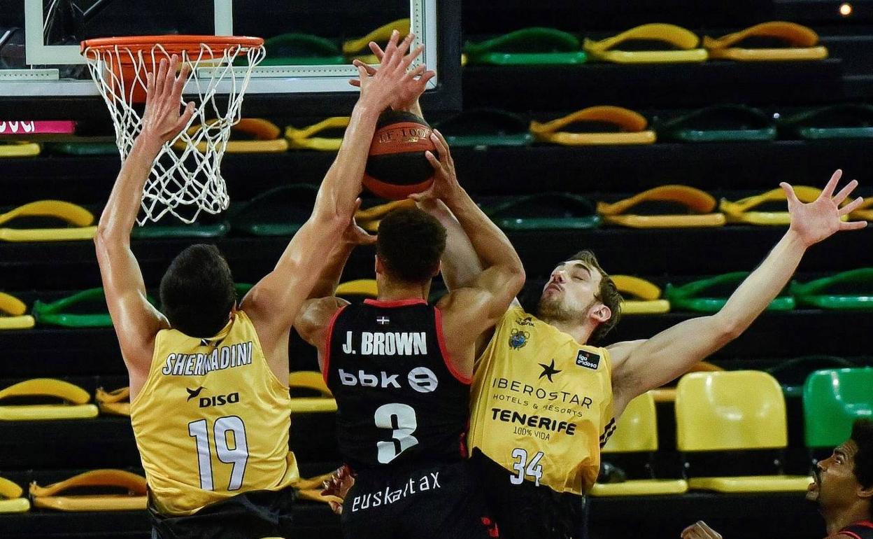 El base estadounidense de Bilbao Basket, Jaylon Brown (c), entra a canasta ante los jugadores de Iberostar Tenerife, el georgiano Giorgi Shermadini (i) y el estadounidense Tyler Cavanaugh, durante el encuentro