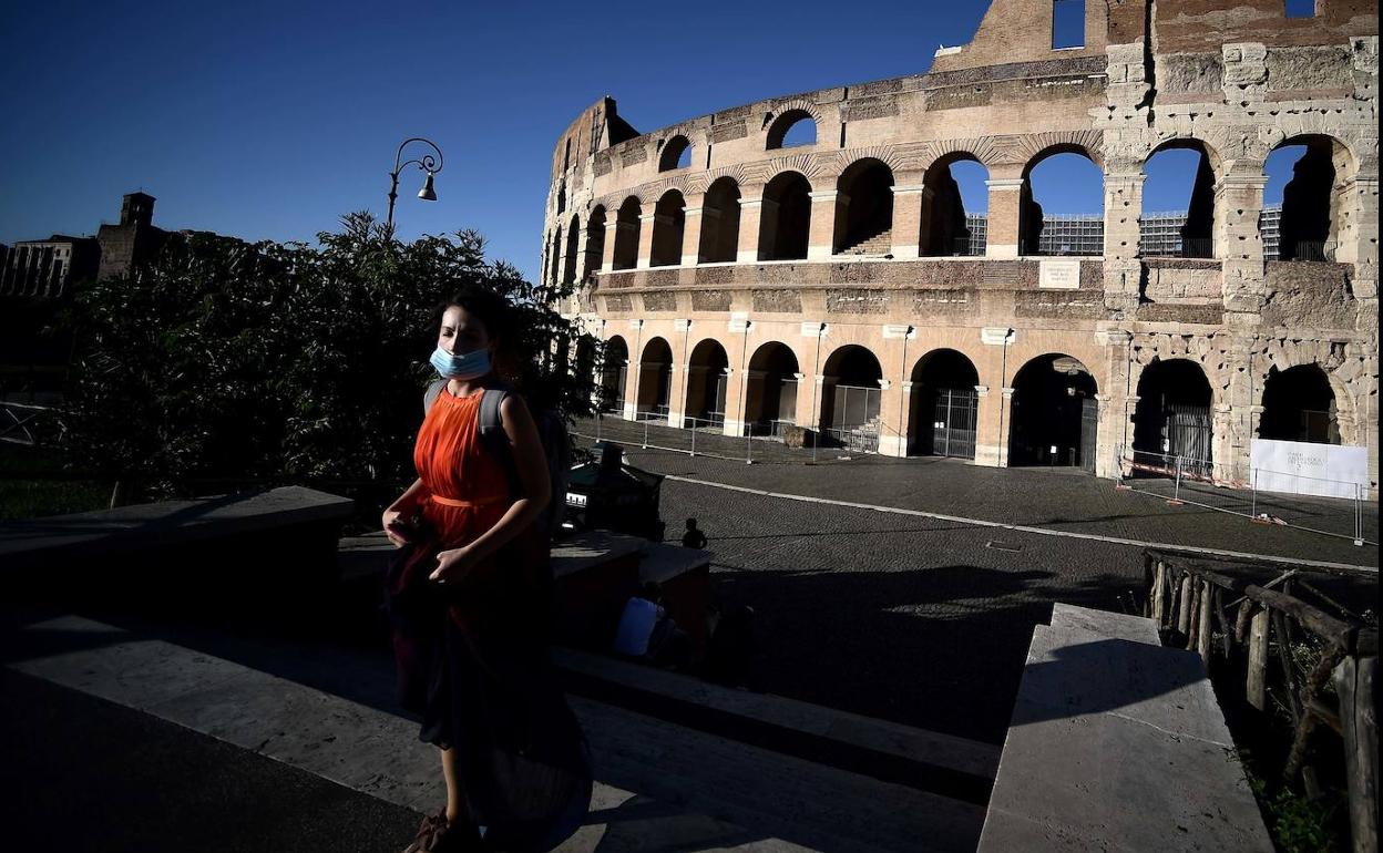 Una mujer protegida con una mascarilla pasea por el centro de Roma, con el Coliseo al fondo. 