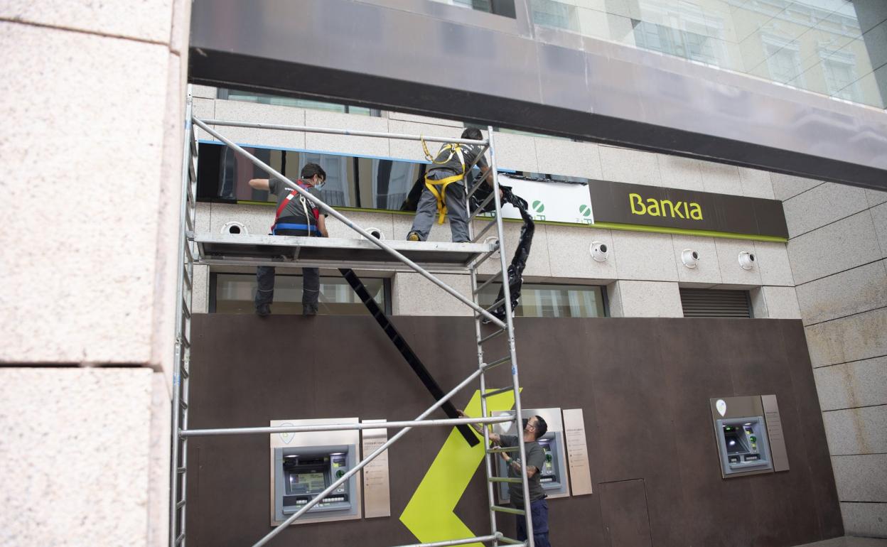 Operarios procedían el lunes a la retirada de la marca Bankia por la de CaixaBank en la sede de la entidad en Triana. 