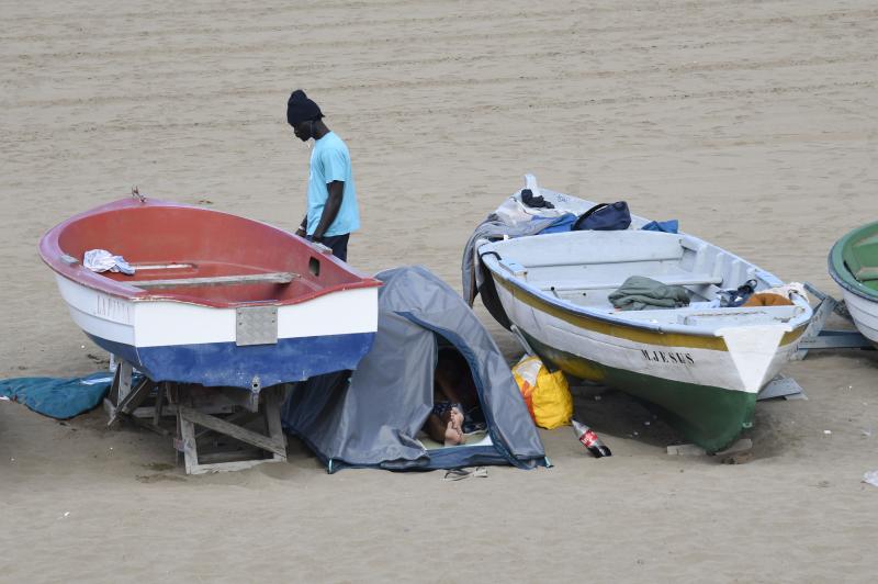 Imagen de personas migrantes en situación de calle acampando en la playa. 