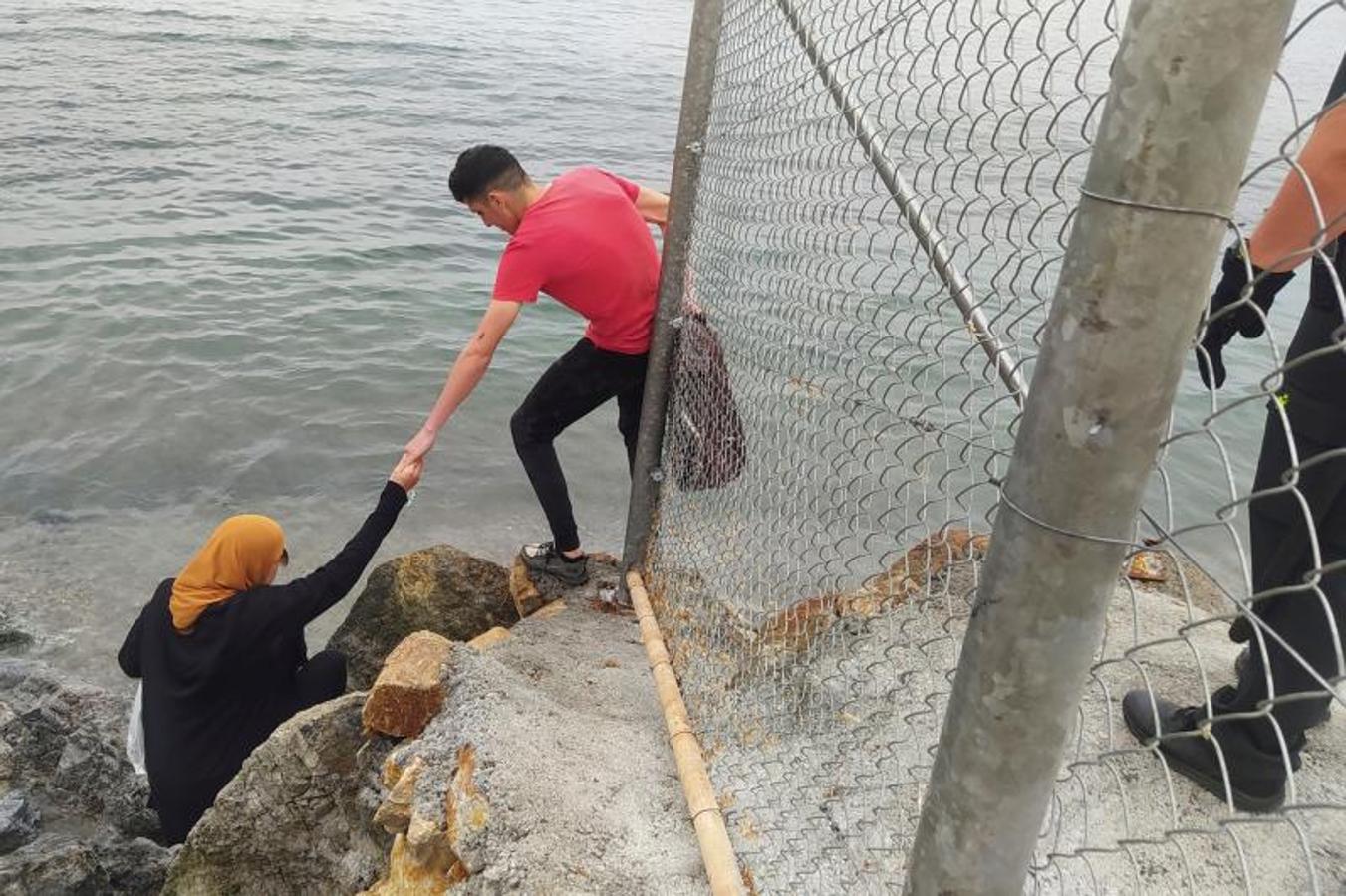 Dos inmigrantes escalan las rocas de uno de los espigones fronterizos de Ceuta.