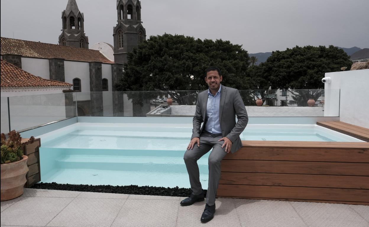 Héctor Suárez posa junto a la piscina de la azotea del Hotel S.XVI con los árboles y la iglesia de la plaza de San Juan al fondo. 