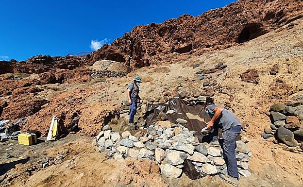 Imagen principal - Foto superior, los arqueólogos cubren las estructuras con una malla geotextil y con piedras para su protección. Debajo, a la izquierda, vista del cantil en cuya falda están los vestigios excavados. A la derecha, escamador hecho de cuerno hallado en el enclave. 