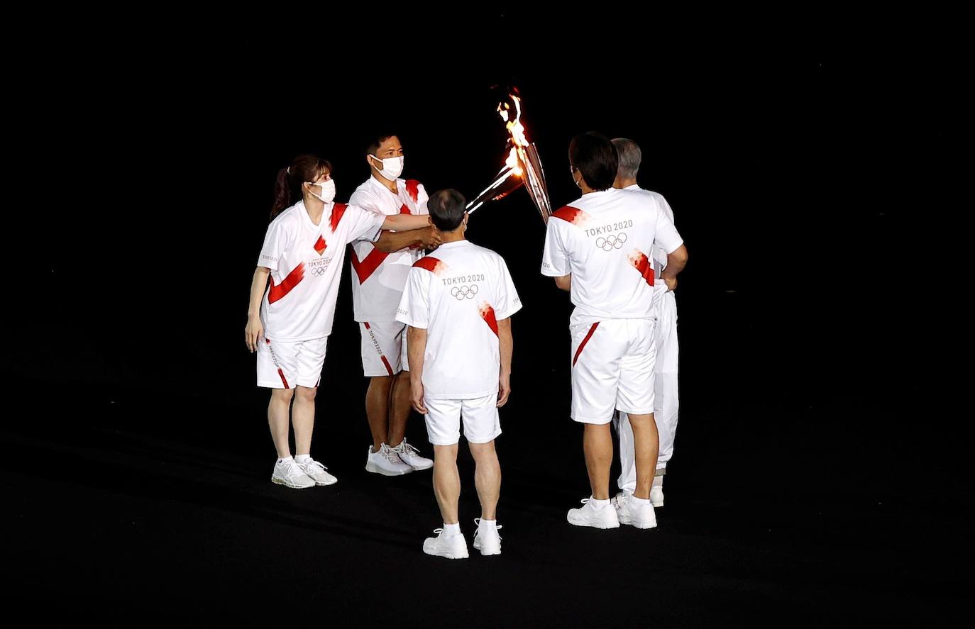 La antorcha olímpica cambia de manos durante la ceremonia de inauguración de los Juegos de Tokio 2020.