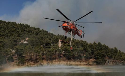 Un helicóptero de los servicios de extinción recarga agua en una área cercana a Atenas. 