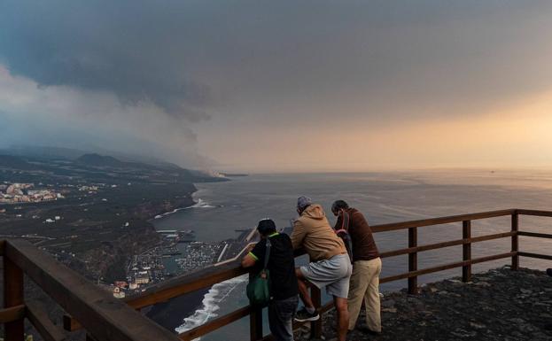 Tres turistas siguen la actividad del volcán palmero desde un mirador en Tazacorte. 