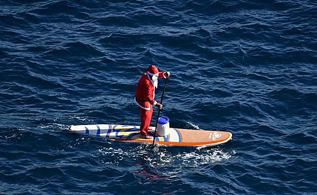 Imagen principal - Papá Noel llega a Arinaga haciendo paddle surf