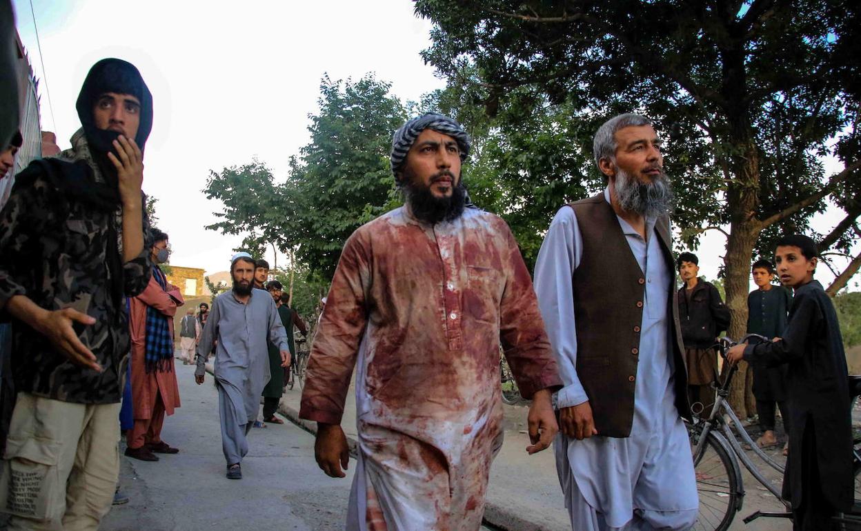 Varias personas, una de ellas con sus ropas ensangrentadas, se alejan del lugar de la explosión en Kabul.