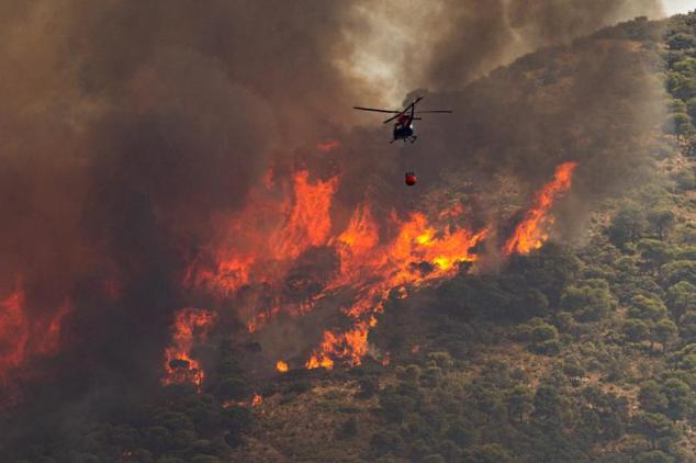 Un helicóptero trabaja en las tareas de extinción del incendio declarado este mediodía en el paraje El Higuerón de Mijas, en Málaga 