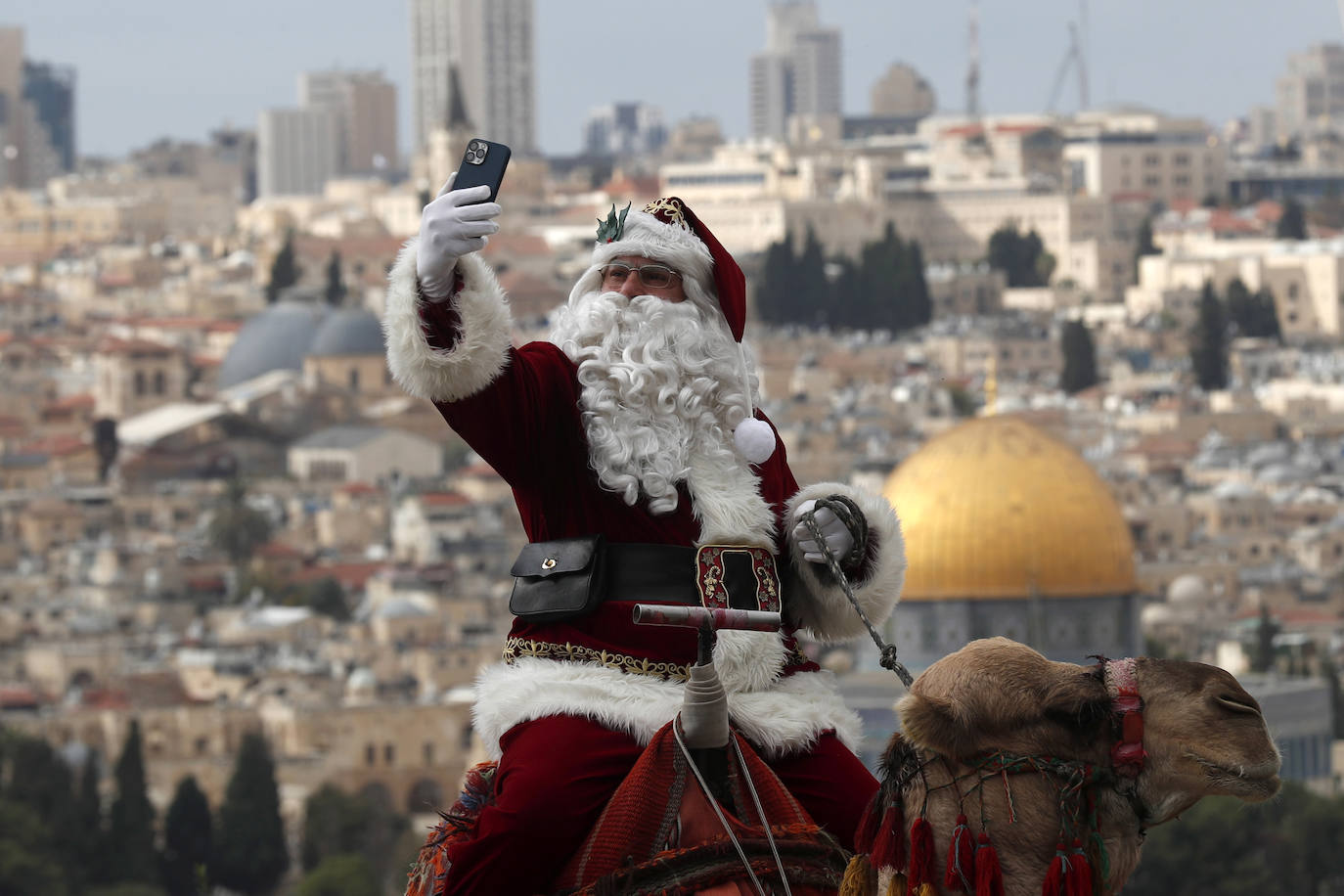 Issa Kassissieh disfrazado de Papá Noel sobre un camello mientras toma un selfie en la Ciudad Vieja de Jerusalén como parte de los preparativos navideños.