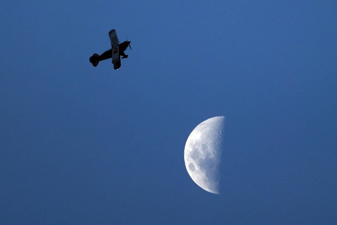 Fotografía de un avión pasando sobre la luna en su fase creciente, desde el estadio Único Madre de Ciudades en un partido amistoso entre las selecciones de Argentina y Curazao en Santiago del Estero (Argentina). 