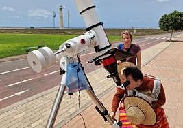 Dos personas miran por el telescopio instalado por el Ayuntamiento de Pájara en la avenida marítima de Solana Matorral, frente a las playas de sotavento de Jandía.