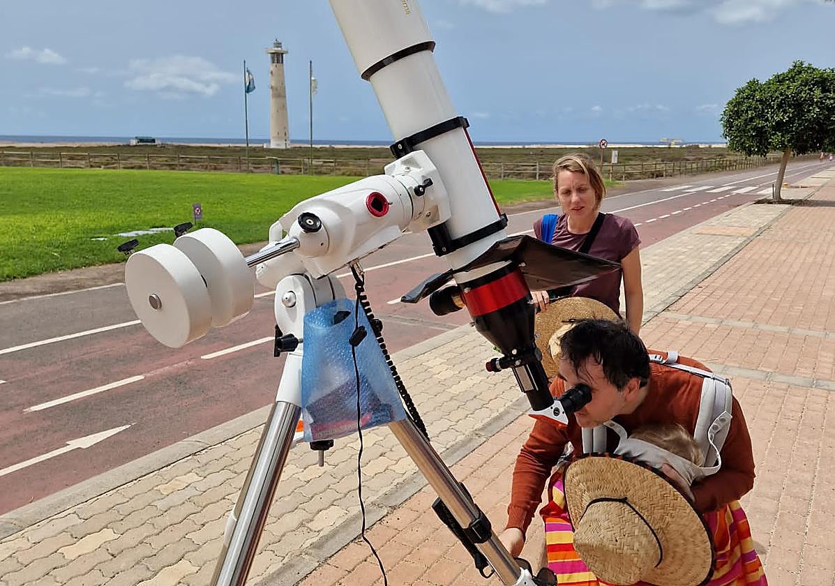 Dos personas miran por el telescopio instalado por el Ayuntamiento de Pájara en la avenida marítima de Solana Matorral, frente a las playas de sotavento de Jandía.