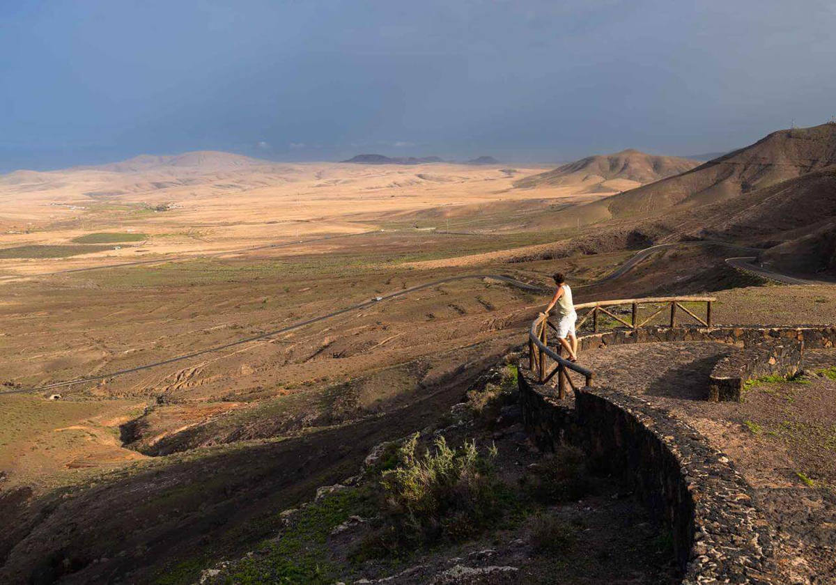Un hermoso atardecer.- Uno de los mejores momentos del día para acercarse a este mirador es al final del día cuando la luz dorada y rojiza tiñe este valle, y permite ver cómo el sol se oculta tras la montaña de Tindaya. Otro de los atractivos de este mirador es su cercanía a la Montaña de la Muda, un lugar de interés histórico, ya que alberga un yacimiento arqueológico perteneciente al pueblo majo, en el que podremos encontrar cuevas, grabados rupestres y pequeñas edificaciones ganaderas.