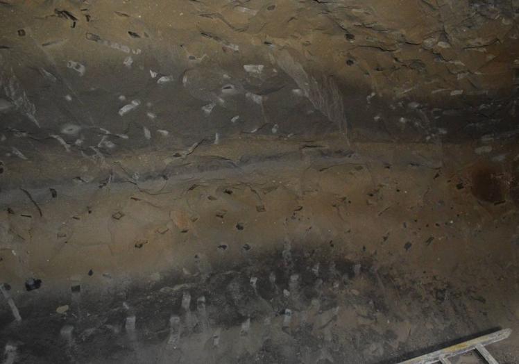 Imagen principal - En la foto superior, pared de la cueva completamente picada. Falta por determinar si esta parte de la pared había grabados. Debajo, zona exterior del resto del yacimiento y puerta anclada en el vano de la cavidad. 