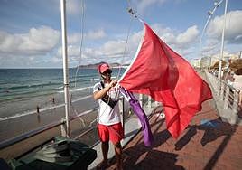 Un voluntario de Cruz Roja iza las banderas lila y roja en Las Canteras.