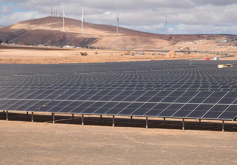 Parque fotovoltaico en las afueras de Puerto del Rosario y compuesto por 12.700 paneles solares. Al fondo, cuatro de los ocho aerogeneradores del parque eólico de Naturgy.