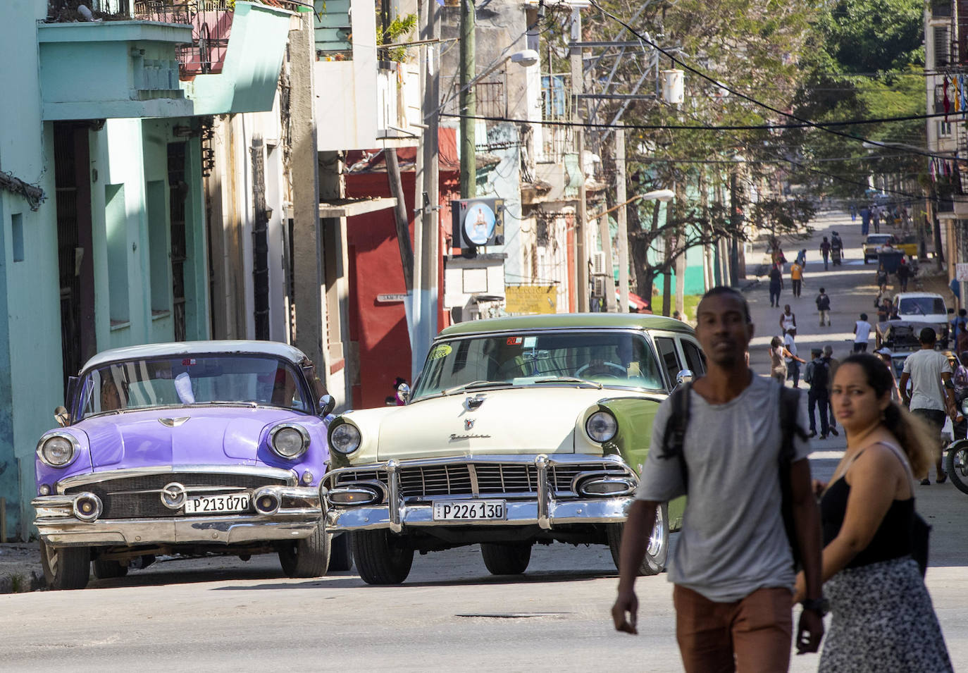 Un grupo de personas camina por las calles junto a dos vehículos clásicos, emblemáticos de la isla cubana, este martes en La Habana. 