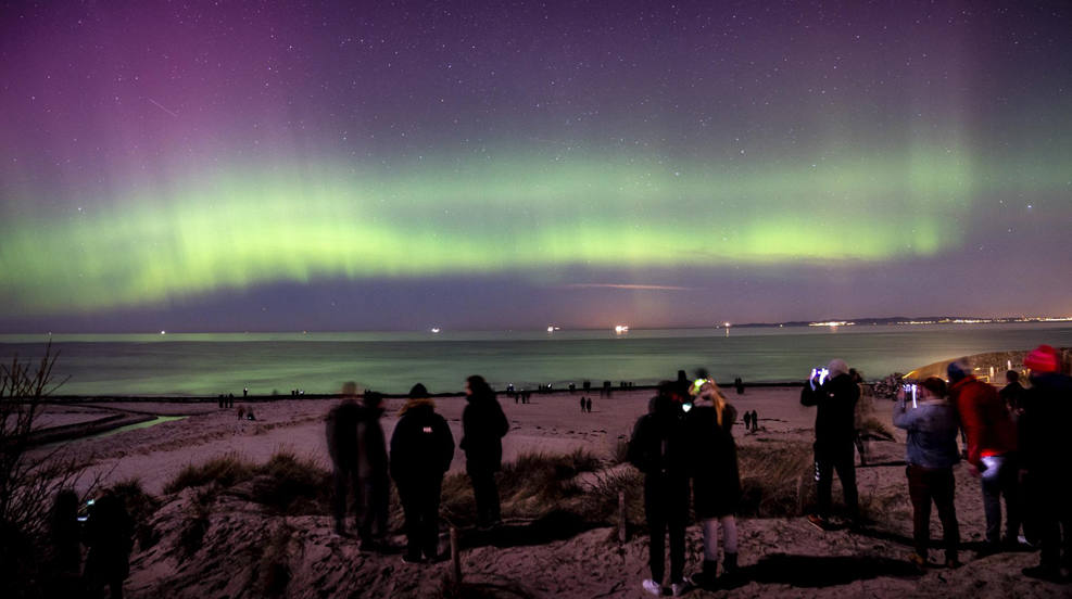 Personas observan la aurora boreal, o aurora boreal, que aparece en el cielo de Dinamarca vista desde Hornbaek Strand en Selandia del Norte, (Dinamarca)